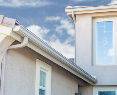close up of a stucco home with white rain gutters - Rain Master Seamless Gutters