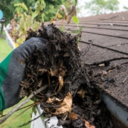 person wearing green glove cleaning gutters - Rain Master Can Clogged Gutters Lead to Foundation Damage?