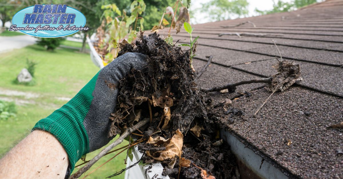 person wearing green glove cleaning gutters - Rain Master Can Clogged Gutters Lead to Foundation Damage?