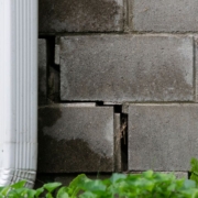 close up of a brick foundation with a crack and a white gutter spout - Rain Master Seamless Gutters