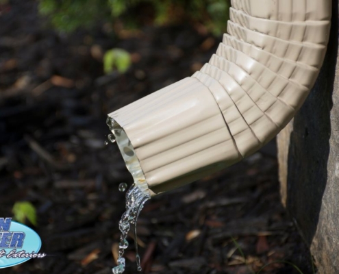 tan colored downspout with water coming out - Rain Master Gutters for Drainage